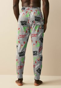 Gray pajama pants with an elastic waistband, featuring a pattern of green roosters and red accents, along with text, "Corn Flakes," and branding.