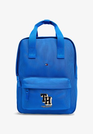 Sac à dos bleu Tommy Hilfiger avec poche avant zippée, doubles poignées, petit logo près du centre supérieur, et grand "TH" brodé sur la poche avant.