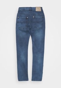 Jeans de mezclilla azul vistos desde atrás, con una cinturilla, dos bolsillos de parche y una etiqueta texturizada en la parte superior de la espalda.