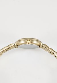 Gold metal wristwatch with a linked band shown from the side, highlighting the crown and watch case against a white background.