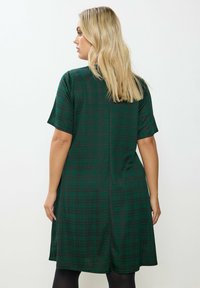 Abito verde a quadri con maniche corte, texture morbida, forma svasata e orlo fino al ginocchio. Il dettaglio sul retro include una cucitura centrale.