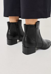 Schwarze Leder-Stiefeletten mit runder Zehenform, seitlichem Reißverschluss und Blockabsatz. Verfügt über elastische Einsätze für Flexibilität und eine glatte Textur.