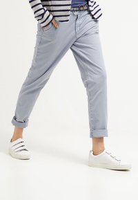 Jasnoniebieskie bawełniane spodnie z podwiniętymi mankietami, slim fit, z bocznymi kieszeniami, noszone z białymi sneakersami z wieloma paskami i płaską podeszwą.