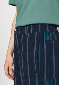 Marinblårandiga shorts med elastisk midja, i kombination med sidofickor, teal-accenter och strukturerad tyg. Stylad med en grön topp.