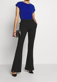 Top corto de manga corta azul, pantalones acampanados negros de cintura alta con aberturas laterales y tacones negros de punta. Incluye un pequeño bolso negro.