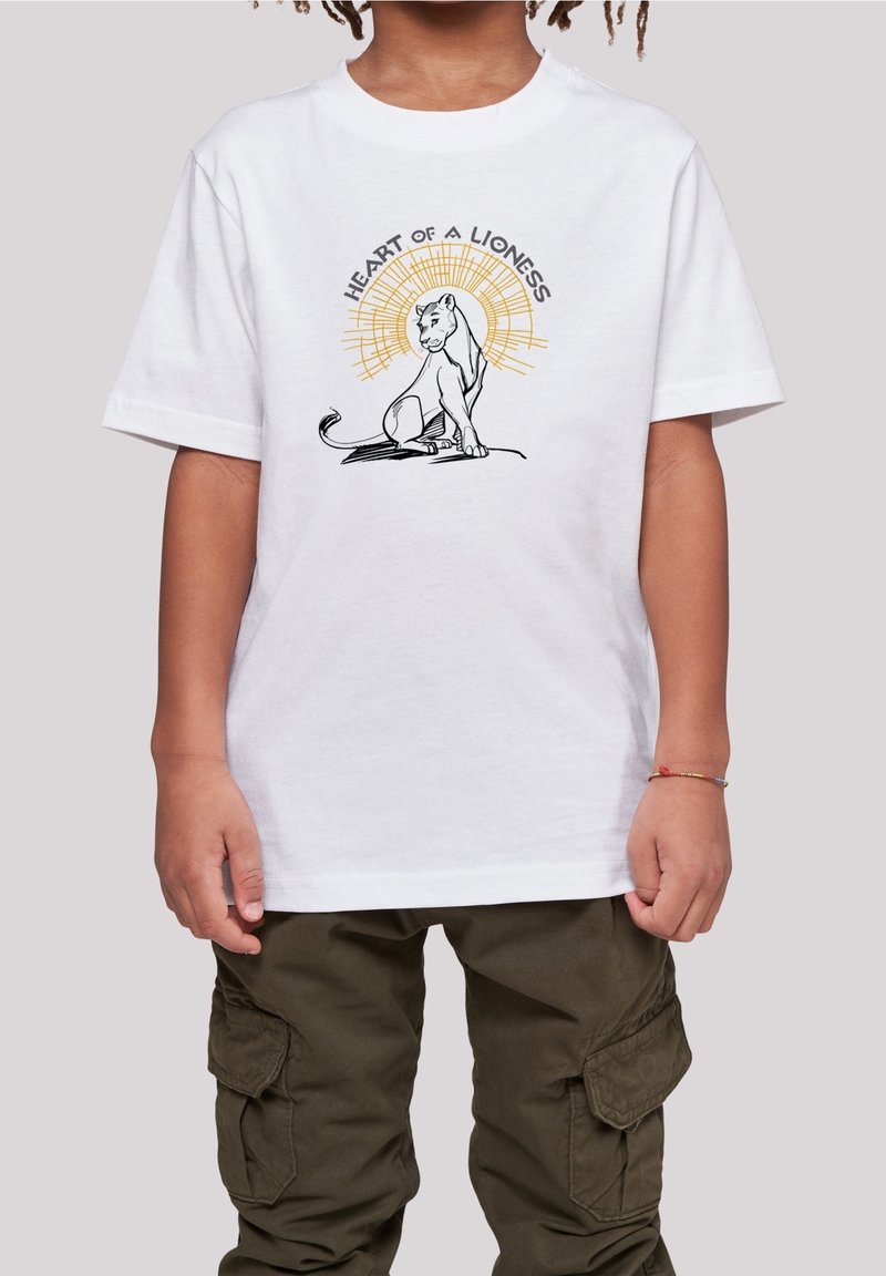 Niño con camiseta blanca con una ilustración de una leona sentada y el texto "Corazón de leona", combinado con pantalones cargo verde oliva.