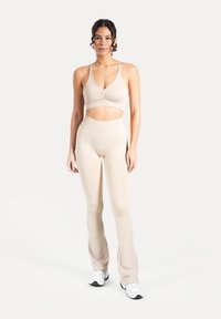 Jasnobeżowy komplet odzieży sportowej składający się z krótkiego topu na ramiączkach z marszczonym detalem oraz legginsów z wysokim stanem i rozszerzanymi nogawkami, wykonany z teksturowanego materiału.