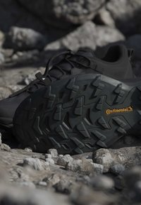 Chaussure de randonnée noire avec semelle Continental robuste reposant sur un sol rocheux en plein air.