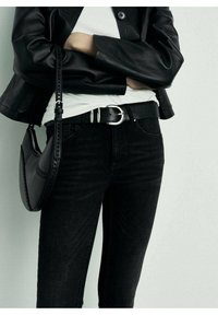 Vaqueros pitillo de mezclilla negra con un cinturón de cuero negro con hebilla plateada, combinados con una camiseta blanca ajustada y un bolso negro de hombro.