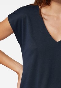 Top blu navy a maniche corte con scollatura a V profonda, caratterizzato da una texture liscia e una vestibilità rilassata. Dettagli di cucitura discreti sulle spalle.