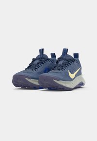 Blå sportskor med en texturerad ovandel, gul swoosh-logotyp, chunky prickig sula och snörningssystem med dragflikar för enkel påklädning.