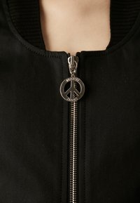 Μαύρο μπουφάν bomber με ασημένιο φερμουάρ και κλείσιμο με σήμα ειρήνης, ριμπ κολάρο και λεία υφή υφάσματος.