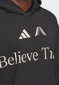 Schwarzer Hoodie mit weißem "Believe That"-Text, weißem Adidas-Logo und Akzenten. Glattes Material, normale Passform und verstellbare Kapuze.