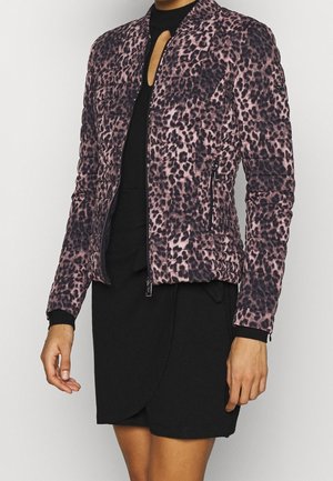 Mujer con una chaqueta ajustada acolchada con estampado de leopardo rosa y negro sobre un vestido negro con escote de ojo de cerradura.