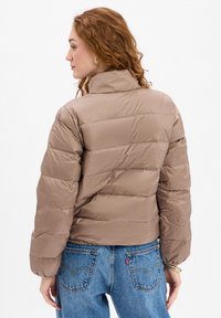 Puszysta beżowa kurtka z poziomym pikowaniem i wysokim kołnierzem. Wykonana z błyszczącego materiału, charakteryzująca się luźnym krojem i lekko skróconą długością.