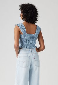 Haut court smocké bleu clair avec des bretelles à volants et un ourlet peplum, associé à un jean bleu clair à jambes larges avec des poches arrière.