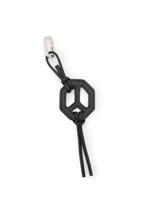 Musta nahkainen avaimenperä, jossa on oktaagonimainen keskipiste, solmittuja lenkkejä ja hopealangallinen klipsi valkoisella taustalla.