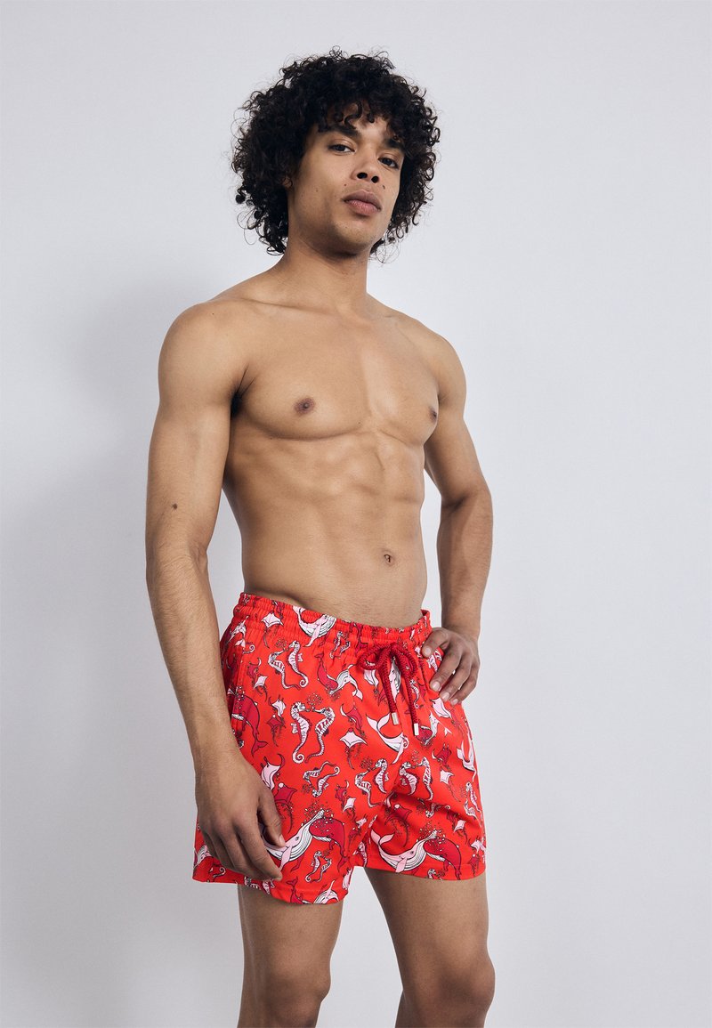 Raudonos maudymosi šortai su žaismingu baltos ir rožinės spalvos jūros arkliuko raštu, su elastinga juosta ir sureguliuojama virvelei tinkamam prisitaikymui.