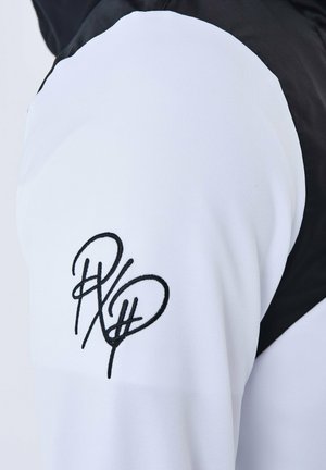 Giacca bianca e nera con un tessuto testurizzato, caratterizzata da un logo ricamato nero prominente sulla manica e un design a blocchi di colore.