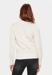 Kremowy sweter dzianinowy z okrągłym dekoltem, długimi rękawami i ściągaczami. Teksturowana tkanina o miękkim wykończeniu i lekkim połysku.