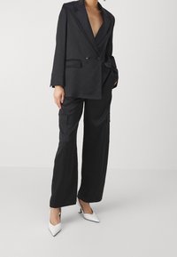 Czarny dwurzędowy blezer z klapami w szpic, zestawiony z luźnymi czarnymi spodniami cargo z bocznymi kieszeniami oraz białymi szpiczastymi szpilkami.