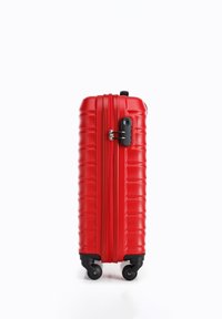 Red hard-shell suitcase with vertical grooves, black zipper and lock, four swivel wheels, and a sturdy handle on top for easy transport.