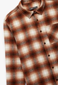 Bruine en crèmekleurige geblokte flanellen shirt met een klassieke kraag, knoopsluiting en een enkele borstzak. Gelaagd stof met een geruit patroon.