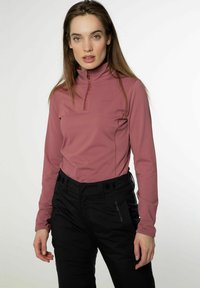 Fitted longsleeve top in zacht roze met een half-rits kraag en subtiele branding. Gepaard met zwarte, gestructureerde broek met zijaccenten.