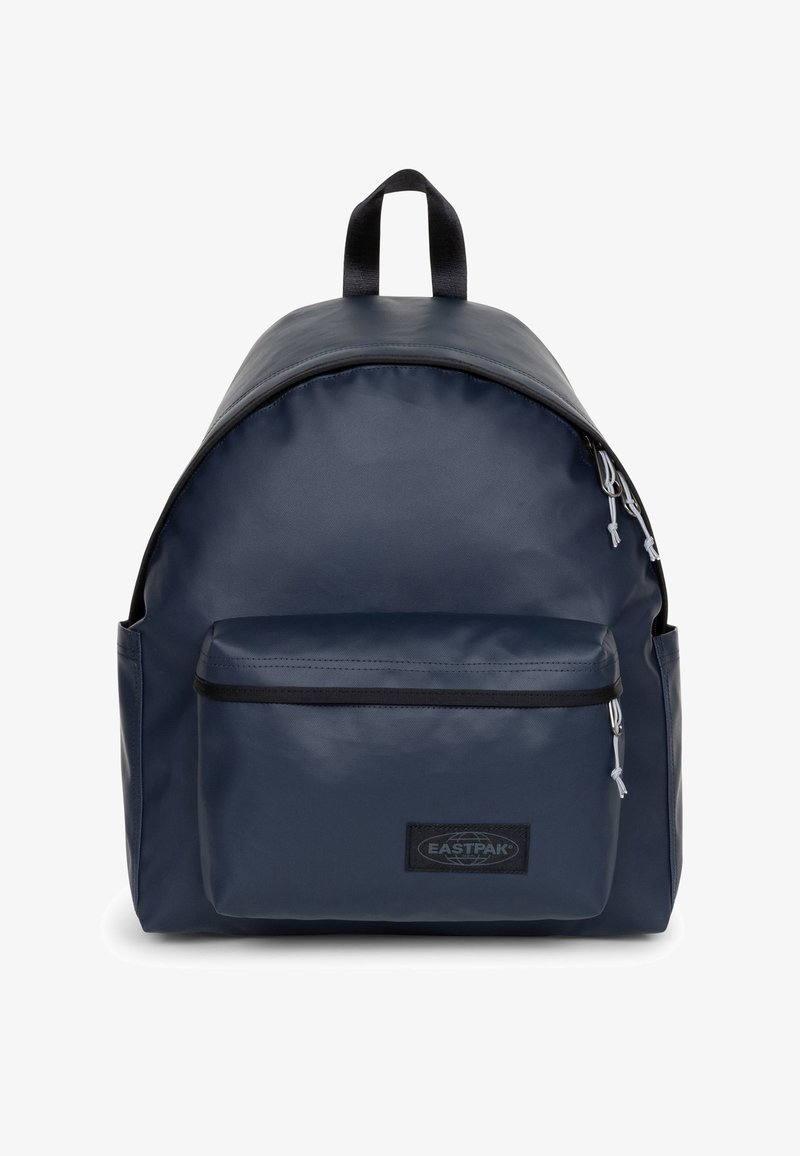 Sac à dos en nylon bleu marine de forme arrondie, avec une poche zippée à l'avant, un patch logo, et deux bretelles réglables. Il possède une poignée de transport sur le dessus.