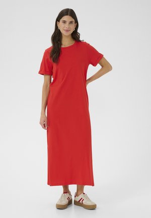 Vestido maxi de algodón rojo con mangas cortas, escote redondo y un corte relajado, combinado con zapatillas beiges que presentan rayas rojas.