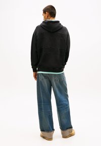 Felpa con cappuccio nera con un design testurizzato, con il nome del marchio impresso in rilievo. Abbinata a jeans denim blu larghi e stivali beige.