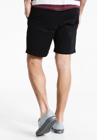 Pantaloni scurți negri din bumbac cu tiv răsucit, asortați cu pantofi din pânză gri deschis, având o talpă texturată și detalii minime de branding.