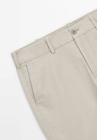 Beiga bomullshängsel med flat front, sidofickor och knappstängning. Har en slät yta och skräddarsydd passform.