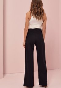 Pantaloni negri cu picioare largi, cu o textură fină și talie înaltă, asortați cu un top alb cu nervuri, adaptat pe corp. Modelul este prezentat din spate.