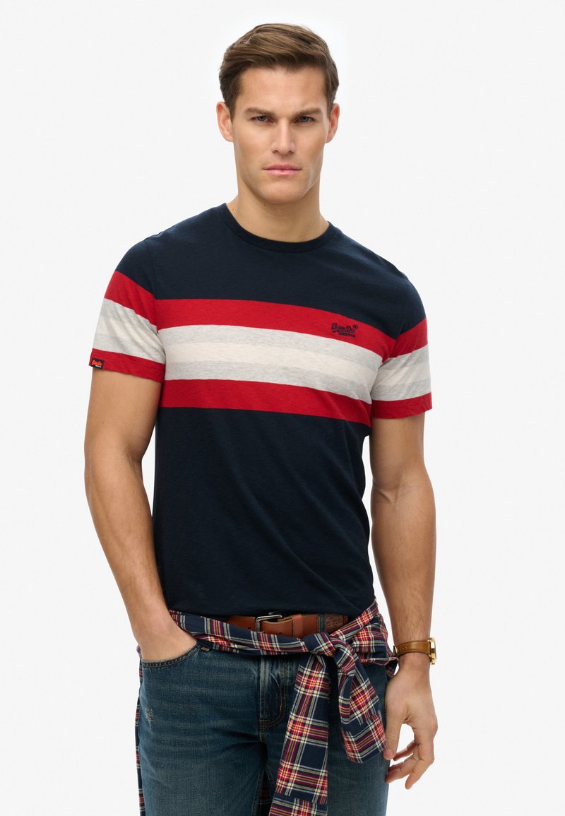 Navy short-sleeve t-shirt with red and gray horizontal stripes, cotton material, worn with rolled plaid shirt tied at the waist, casual fit.