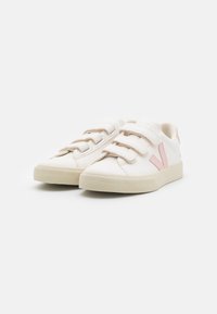 Hvit sneakers med tre borrelåser, rosa detaljer, en teksturert gummisåle og en glatt syntetisk overdel. Minimalistisk design.