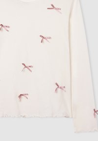 Top a maniche lunghe di colore crema con piccoli fiocchi di raso rosa sparsi e orlo arricciato sulle maniche e sul fondo.