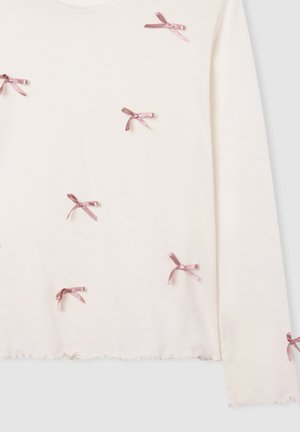 Top a maniche lunghe di colore crema con piccoli fiocchi di raso rosa sparsi e orlo arricciato sulle maniche e sul fondo.