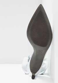 Chaussure à talons hauts bleu clair avec un bout pointu, tige en satin lisse et semelle noire texturée. Présente un petit logo à l'extérieur.