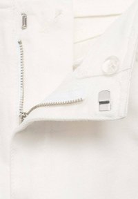 Witte denim stof met een gedeeltelijk open zilveren rits en zilveren haak-en-oogsluiting op een tailleband met een doorzichtige knop.
