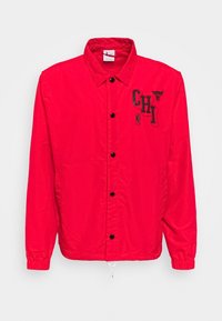 Rode nylon jack met een drukknoopsluiting, zwarte opdruk "CHI" en een bulllogo op de linkerborst. Elastische manchetten en een trekkoord onderkant.
