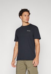 Tricou din bumbac negru cu mânecă scurtă, cu decolteu rotund și un mic logo alb Columbia pe piept, însoțit de șorturi de culoare deschisă.