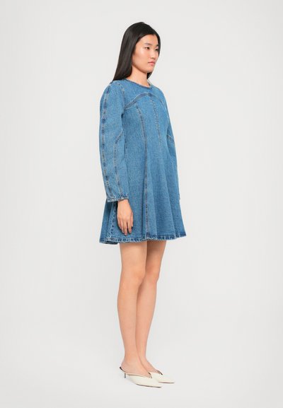 Denimová šaty s dlhými, nadýchanými rukávmi, A-silhueta a nerovný lem. Svetlo modrá farba s viditeľnými švami a okrúhlym výstrihom. Minimalistický dizajn.