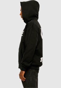 Hoodie noir avec une poche kangourou spacieuse, une grande capuche à cordon et un texte logo blanc à l'avant et à l'arrière. Tissu épais et doux.