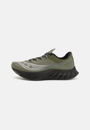 Zapatilla deportiva para correr de color verde y negro con una parte superior de malla texturizada, suela negra y cordones negros, mostrada de lado sobre un fondo blanco.