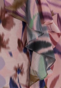 Tissu doux avec motif abstrait aquarelle dans des tons de rose, violet, vert et bleu, présentant des plis superposés et froncés.