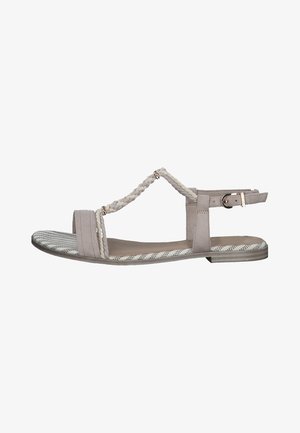 Vaaleanharmaa sandaali, jossa on punotut hihnat, litteä pohja ja nilkkaremmi soljella. Kuvioitu sisäpohja sisältää kuvioidun designin hienovaraisine raidoituksineen.