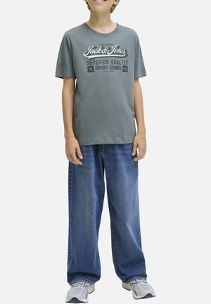 T-shirt en coton gris avec texte et logo blancs, associé à un jean en denim bleu à coupe ample. Coupe décontractée avec manches courtes et col rond.