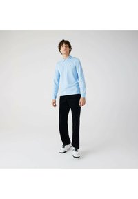 Lyseblå langærmet polo skjorte med krave, kombineret med sorte bukser og hvide sneakers. Har et lille grønt logo på brystet.