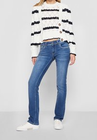 Blå denimjeans har en slim fit och femfickorsdesign, i kombination med en vit och marinblå randig stickad cardigan med knappar.